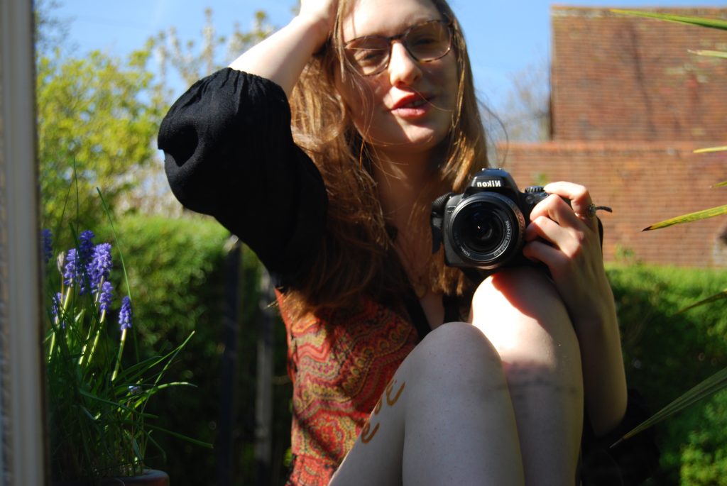 A slightly unfocused image of Sakara pushing back medium length gold brown hair and smiling as though she's in the middle of saying something.