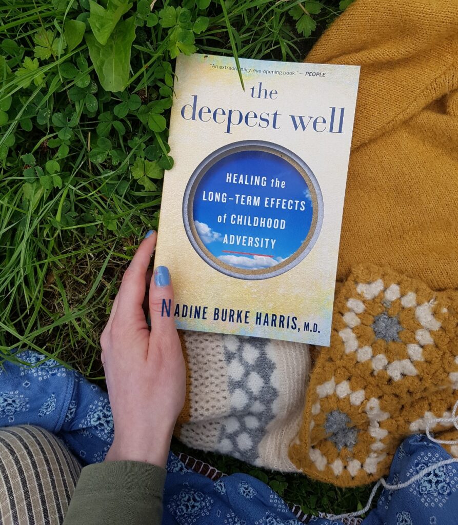 A photo of the paperback book lying on a jumper and some grass outside.