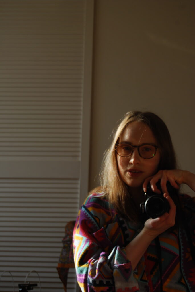 A further selfie of Sakara from the same day, she wears a brightly coloured thick and cosy shirt and gentle sunlight is touching half her face and one arm.