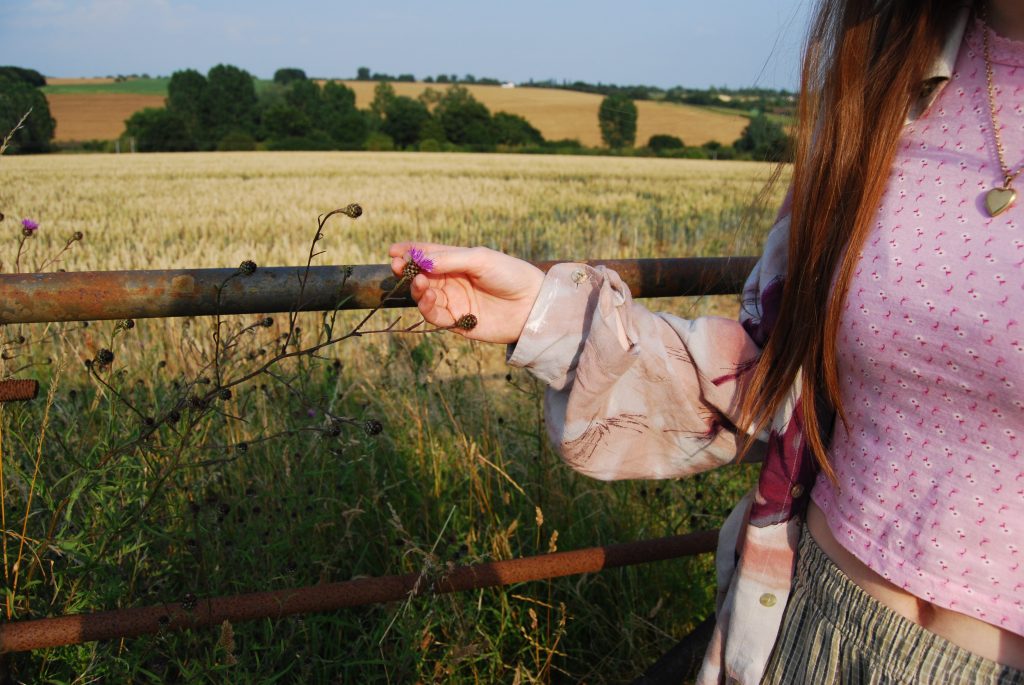 a small, white hand holding a purple thistle flower.