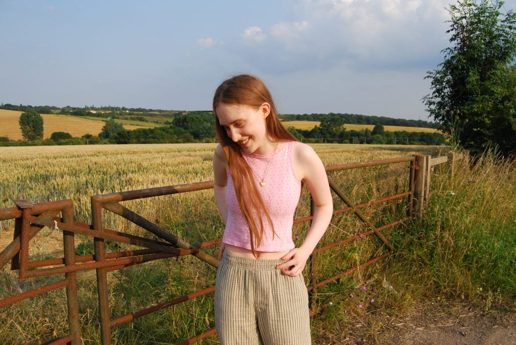 Image: Sakara stands in front of a gate to a large field