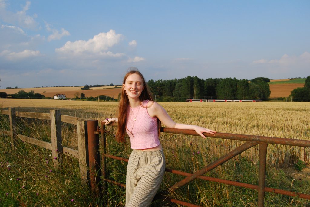 Sakara leans on the gate with an arm spread out either side of her body, she looks comfortable and happy.
