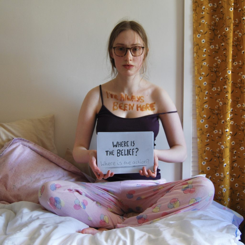 Sakara holds another sign asking two questions: where is the belief and where is the action?