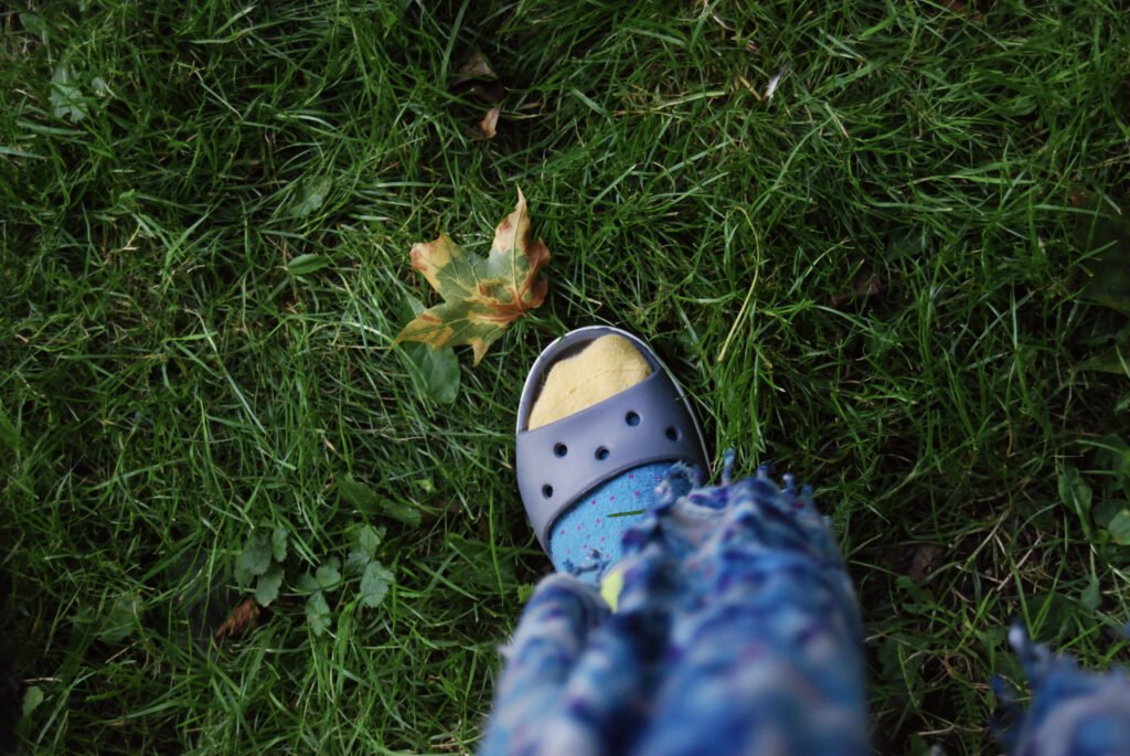 A foot wearing a sandal and sock next to a fallen leaf.