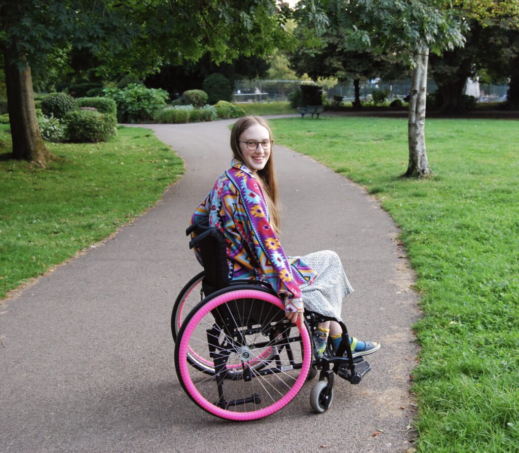 Another wheelchair photo of Sakara smiling at the camera.