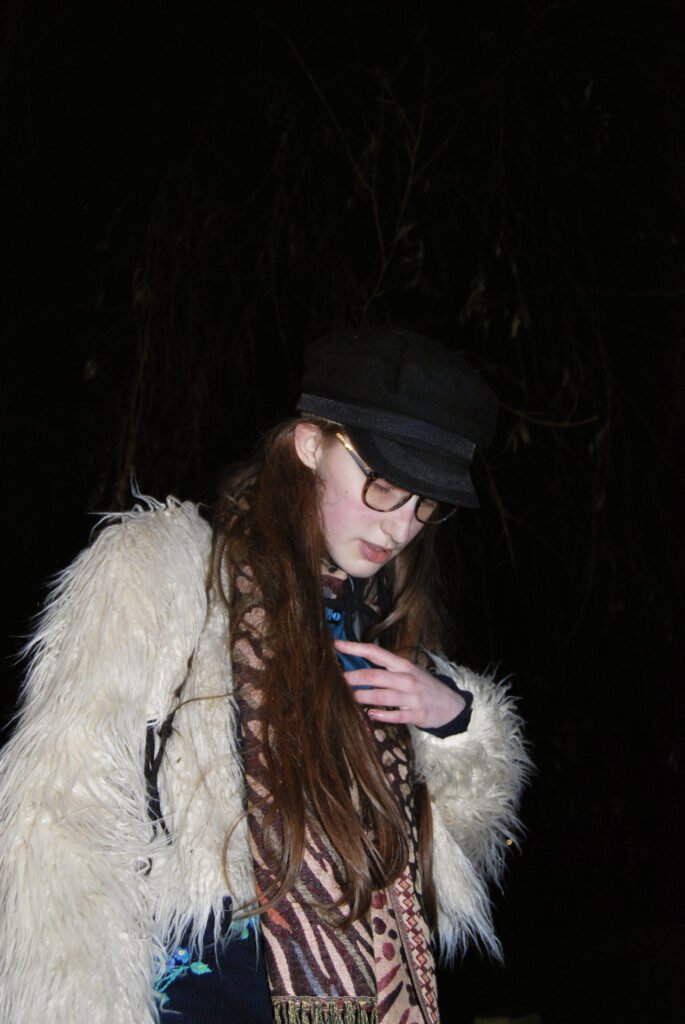 Image: Sakara looks down. She wears a fluffy jacket.