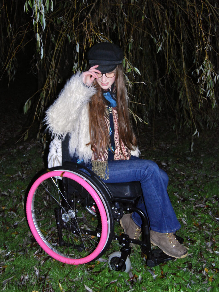 image of Sakara using their wheelchair with a fluffy jacket on.