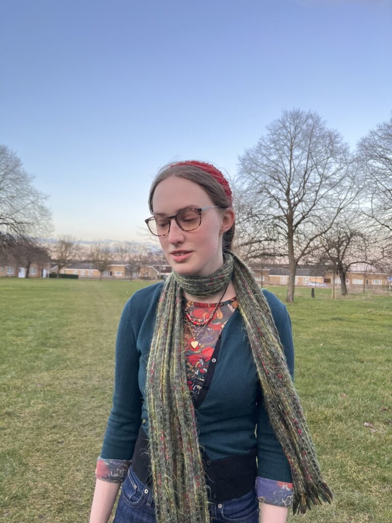 Sakara looks down, her green scarf blows in the breeze.