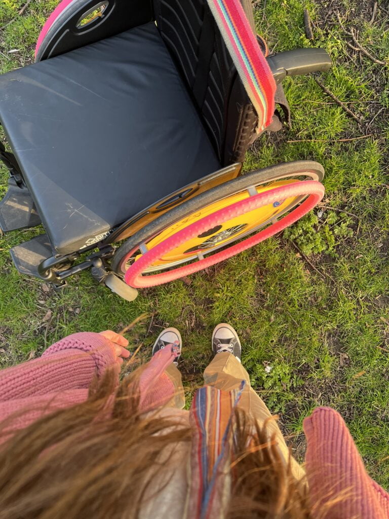 A photo taken from above the wheelchair showing Sakara standing next to it wearing black converse.