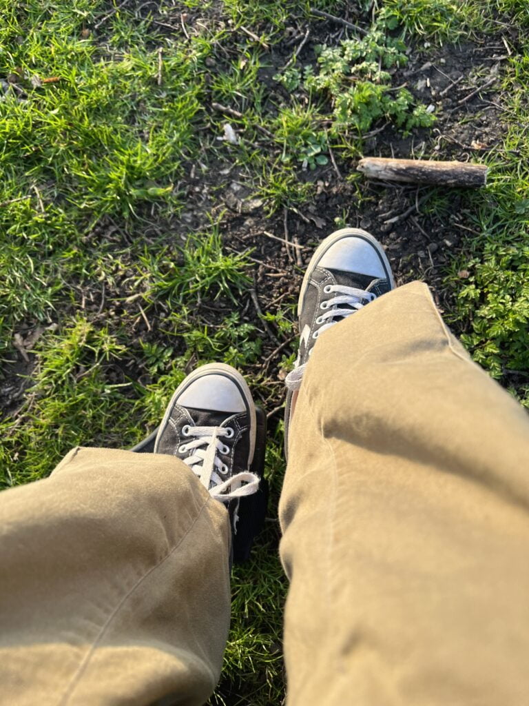 Sakara's trousers and shoes photographed resting on the wheelchair footplate above the grassy ground.