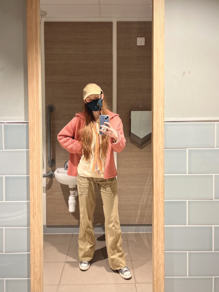 A mirror selfie taken in a supermarket toilet. Sakara stands up and looks at her blue phone.